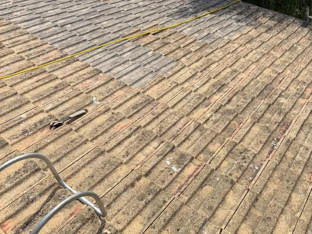 A cleaned roof slope of brown concrete tiles, with a hose and roof ladder on it.