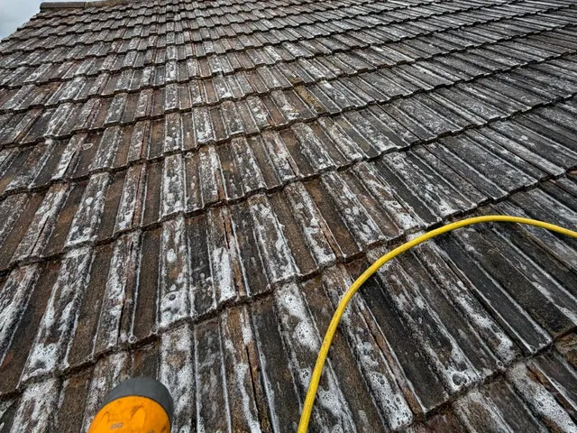 Grey concrete tiles covered in white foamy patches, a yellow hose curving across them.